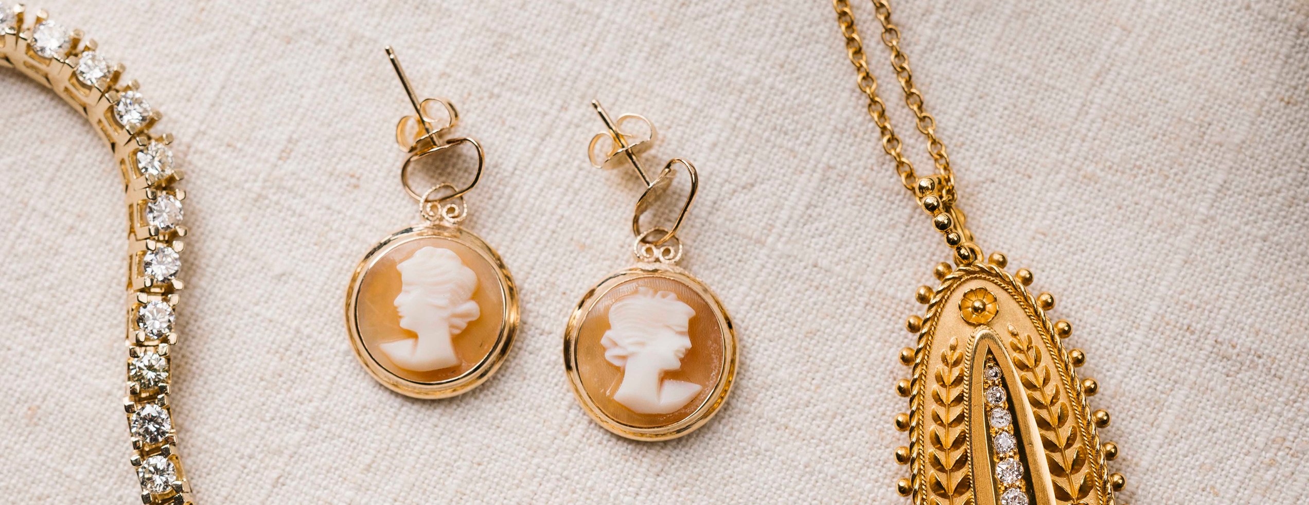 Vintage and estate jewelry from Perry’s: a diamond line bracelet, cameo earrings and a gold locket on linen
