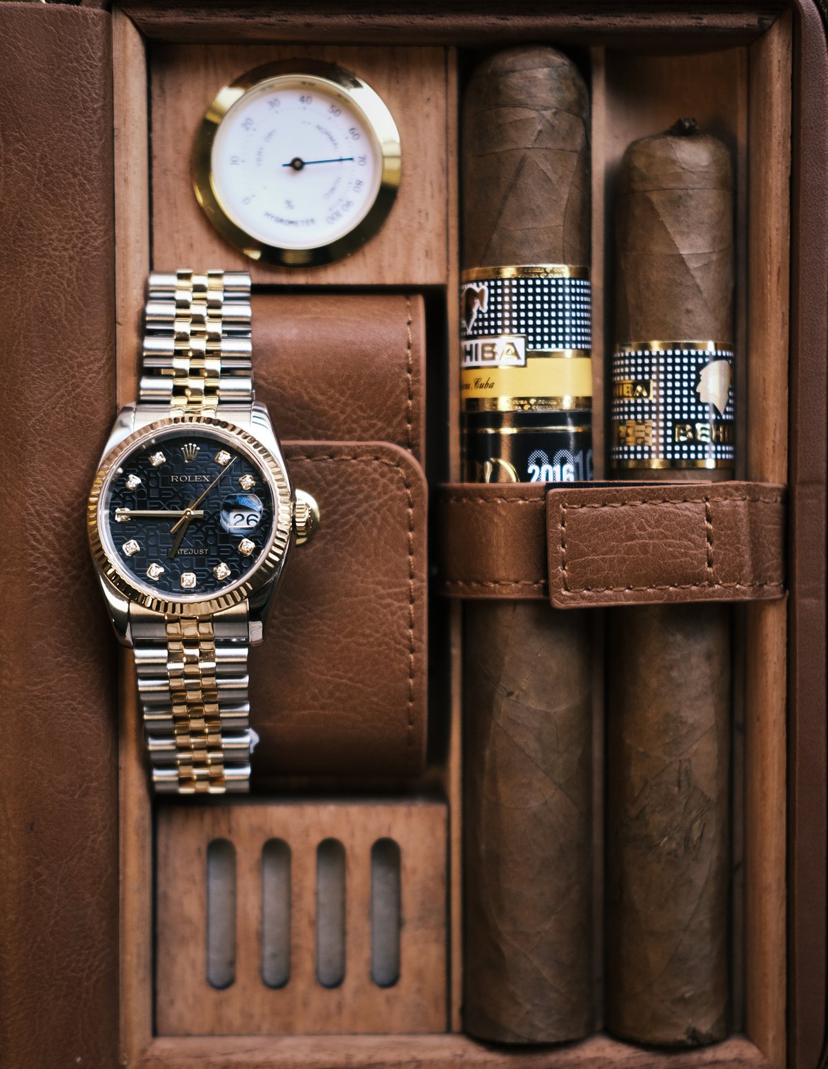 A two-tone Rolex Datejust in a leather case beside two cigars