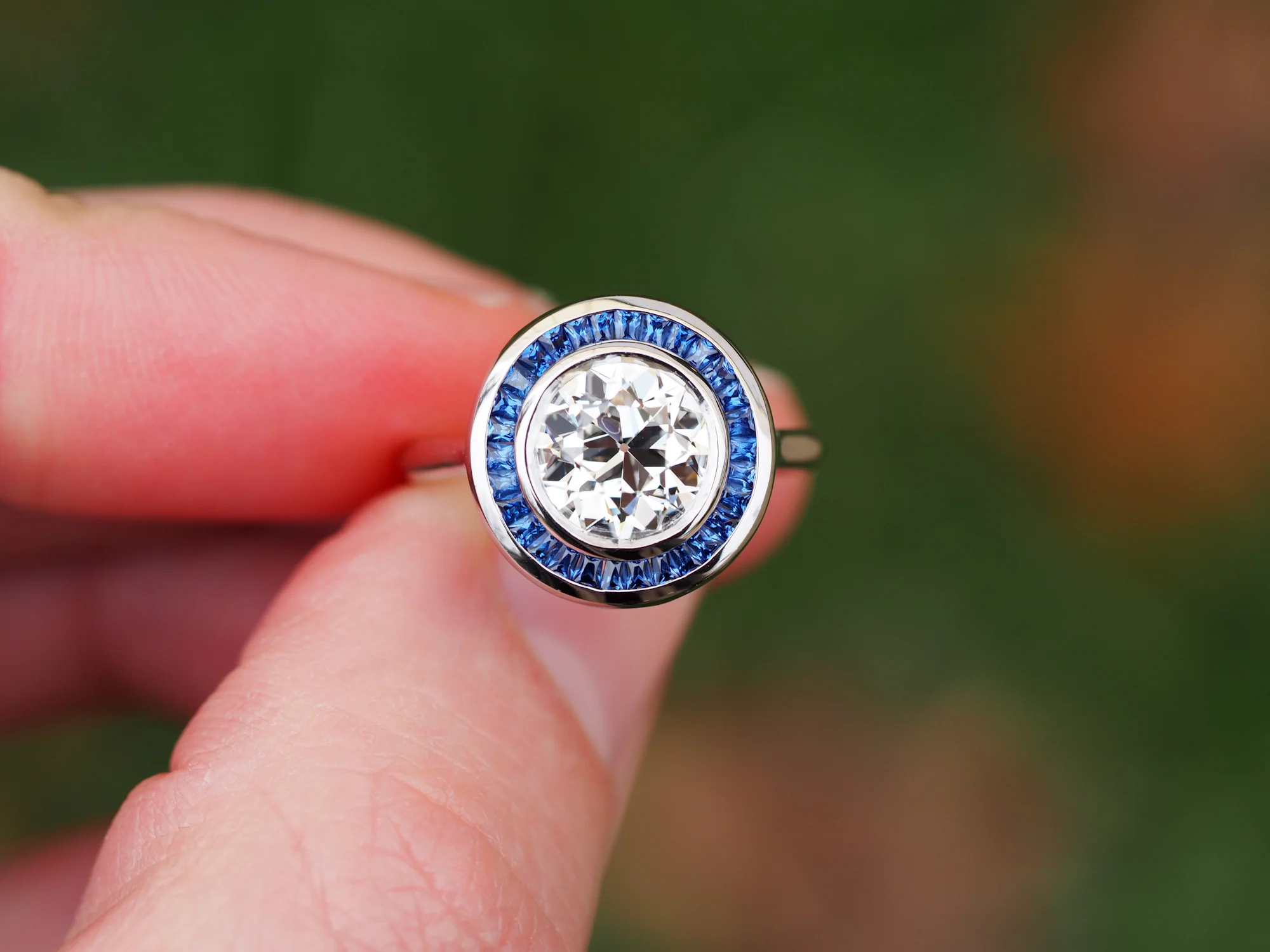 A custom diamond ring with a calibre cut sapphire halo, held in hand