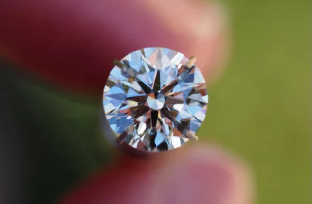 A loose round brilliant cut diamond held between two fingertips